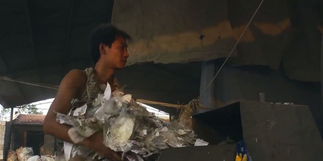 Der Recyclingwerkstattbesitzer Kun füttert Plastik in eine Maschine.
