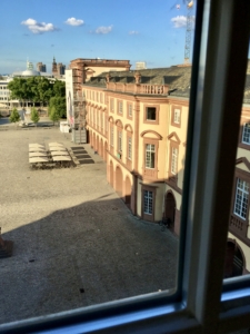 Blick aus dem Fenster der Universitätsbibliothek auf den Ostflügel des Ehrenhofs. Die Sonne steht tief am Ende eines warmen Sommertages. Der Himmel ist Blau über den Dächern der Stadt.