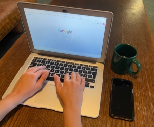 Laptop auf dem Tisch, Handy und Kaffeetasse stehen daneben, Google Suchleiste ist geöffnet