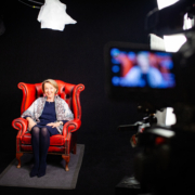 Dreharbeiten zu Eva Umlaufs interaktivem Zeugnis. Das Bild zeigt sie sitzend in einem Sessel, während sie von einer Studiokamera gefilmt wird. England, 2019. (c) Bright White Ltd