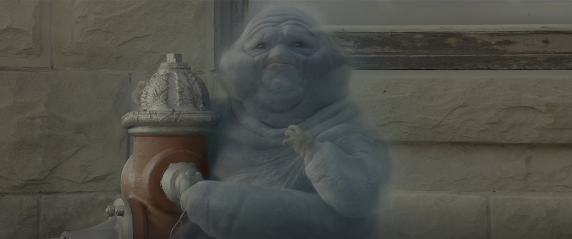 Der Screenshot aus Ghostbusters:Legacy (2021, USA) zeigt den bläulich dursichtigen dickeren Geist Muncher, der neben einem Hydranten. Auf dem Hydranten sind Kratzspuren vom Geist. Er hat hat Appetit auf Metall und hat darauf rumbebissen.