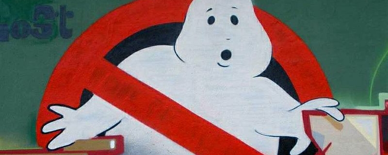 Das Ghostbusters-Logo zeigt einen freundlichen, weißen Geist mit einem überraschten Gesichtsausdruck, der von einem roten Verbotsschild durchkreuzt wird. Der Geist, der leicht comicartig und rundlich gestaltet ist, hebt eine Hand in einer abwehrenden Geste, während das rote, diagonale Verbotssymbol deutlich signalisiert, dass Geister unerwünscht sind.
