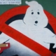 Das Ghostbusters-Logo zeigt einen freundlichen, weißen Geist mit einem überraschten Gesichtsausdruck, der von einem roten Verbotsschild durchkreuzt wird. Der Geist, der leicht comicartig und rundlich gestaltet ist, hebt eine Hand in einer abwehrenden Geste, während das rote, diagonale Verbotssymbol deutlich signalisiert, dass Geister unerwünscht sind.